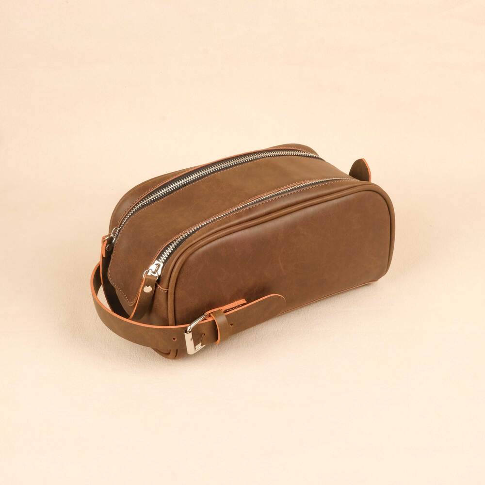 Brown leather toiletry bag with zippers on a beige background