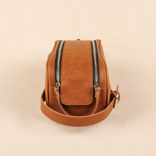 Brown leather crossbody bag with zippers on a beige background