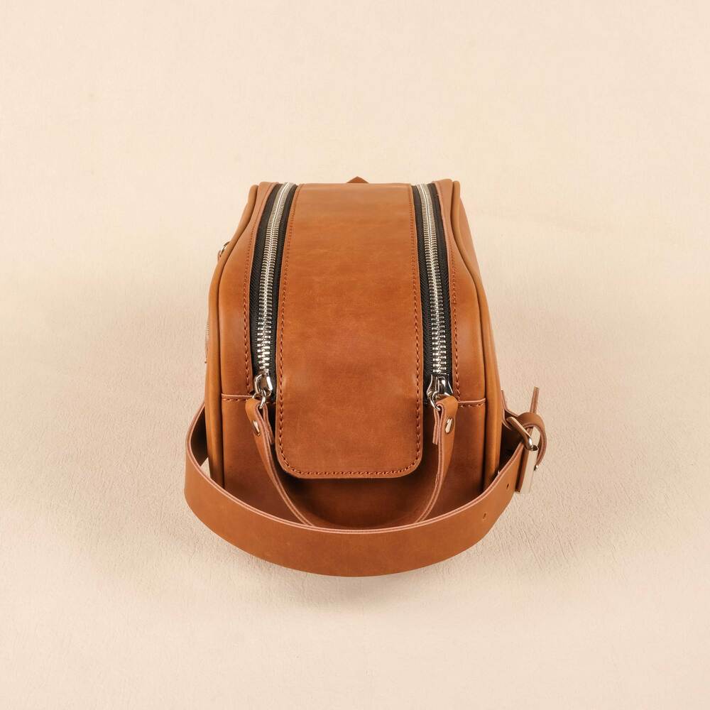 Brown leather crossbody bag with zippers on a beige background