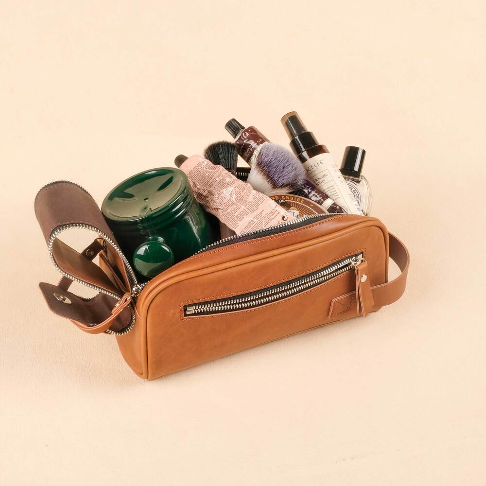 Brown leather toiletry bag with various items on a beige background