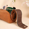 Brown leather cosmetic bag with a strap, containing a green jar and brush, on a beige background with floral elements.
