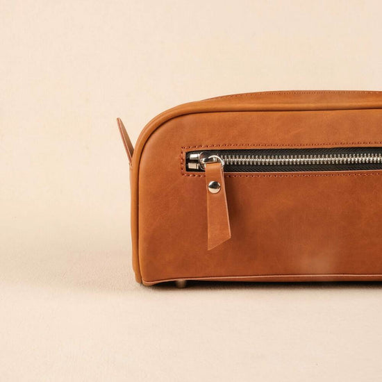 Brown leather toiletry bag with zipper on a beige background