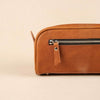 Brown leather toiletry bag with zipper on a beige background