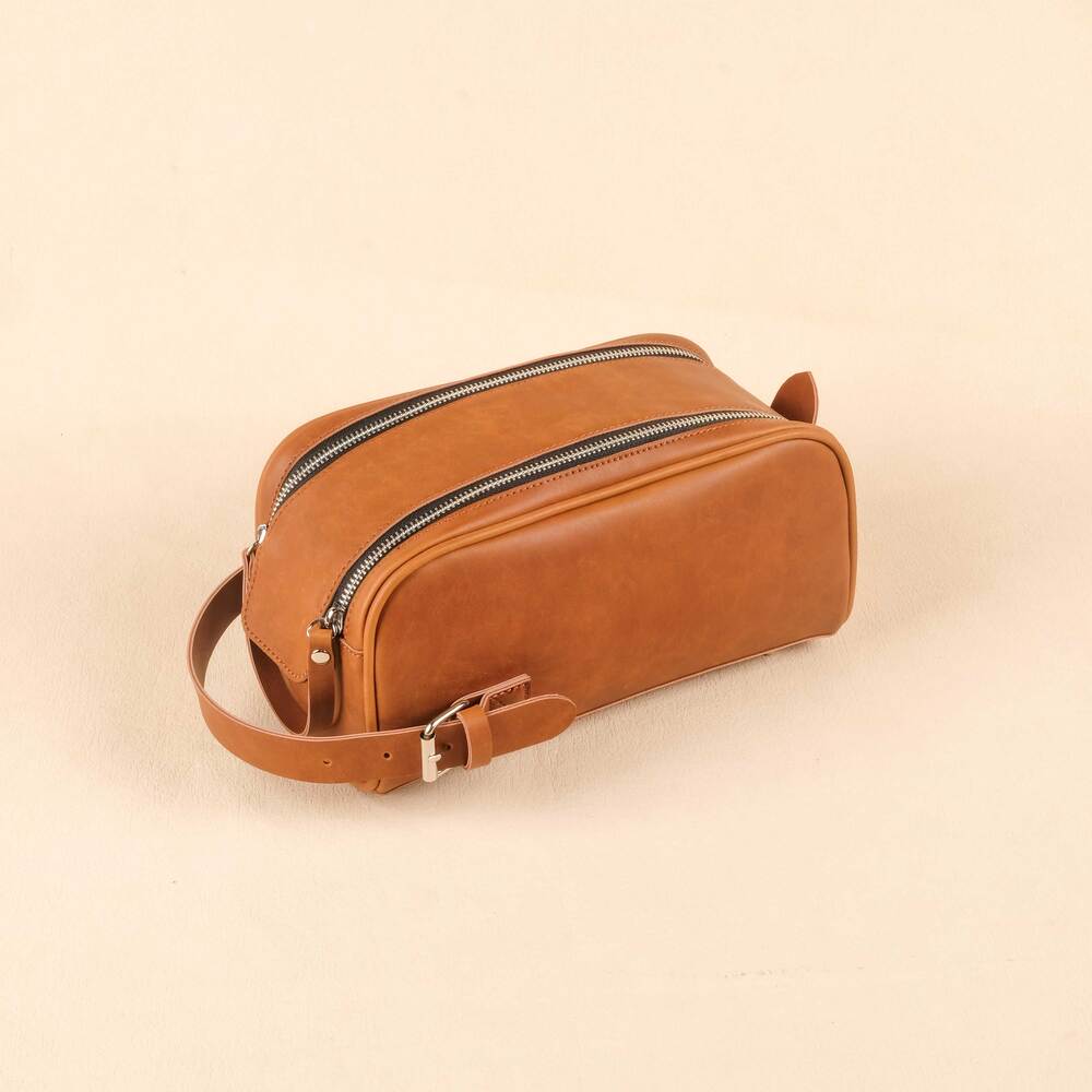 Brown leather toiletry bag with a zipper on a beige background