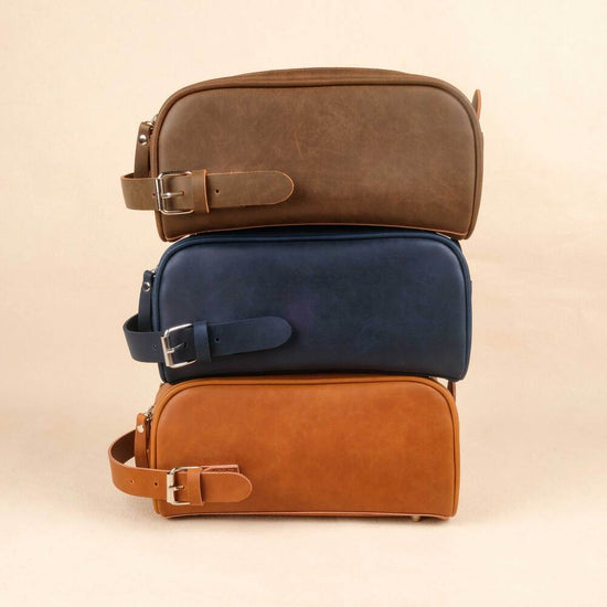 Three leather toiletry bags stacked on a beige background