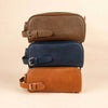 Three leather toiletry bags stacked on a beige background