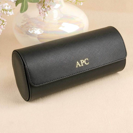 Black sunglasses case with 'APC' branding on a beige surface with floral elements.