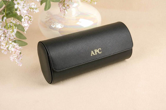 Black sunglasses case with 'APC' branding on a beige surface with floral elements.