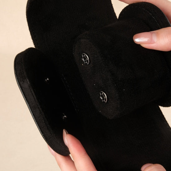 Black plush toy resembling a dog held by a hand against a beige background