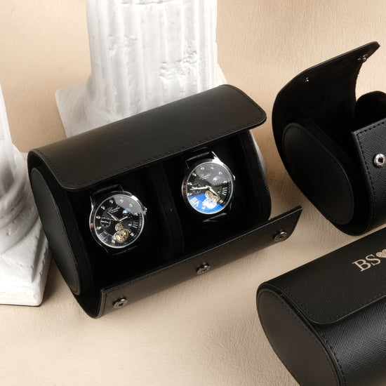 Black watch winder with two watches and a matching case on a beige surface.