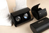 Black watch winder with two watches and a matching case on a beige surface.