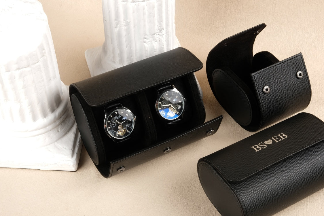 Black watch winder with two watches and a matching case on a beige surface.