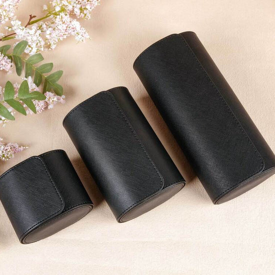 Three black cylindrical containers on a beige surface with floral elements.