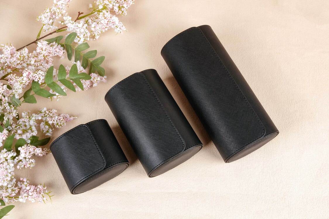 Three black cylindrical containers on a beige surface with floral elements.