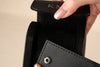 Close-up of a person holding a black wallet with 'KIM' branding.