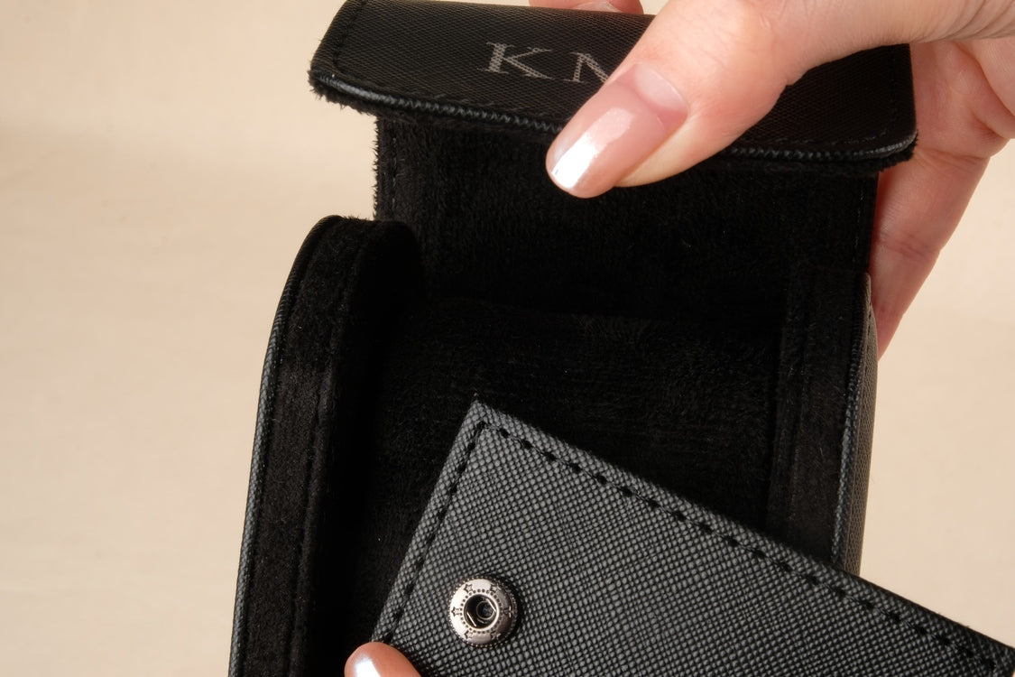 Close-up of a person holding a black wallet with 'KIM' branding.