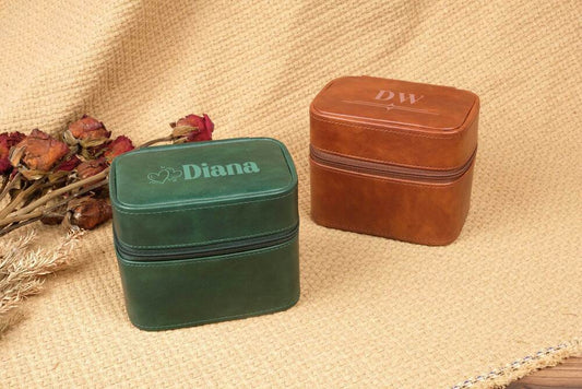 Two jewelry boxes, one green and one brown, on a textured surface with dried flowers.