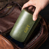 Green leather case with 'GIFT' text held by a hand over an open brown leather bag.