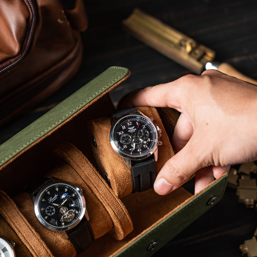 Hand selecting a watch from a brown leather watch box with another watch inside.