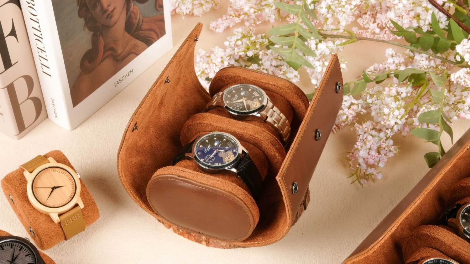 Three watches in a brown leather case on a light surface with flowers and a photo frame in the background.